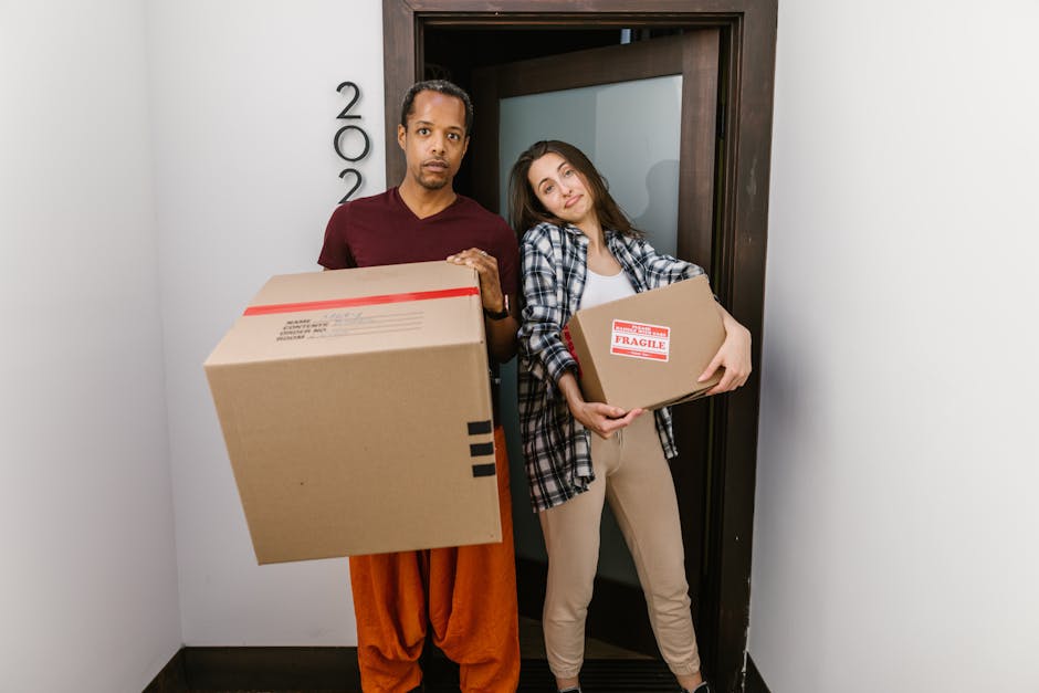 A man and woman standing on the front doorstep of a house during a home relocation, with the man holding a cardboard box and the woman holding a potted plant, preparing for furniture transport and pac